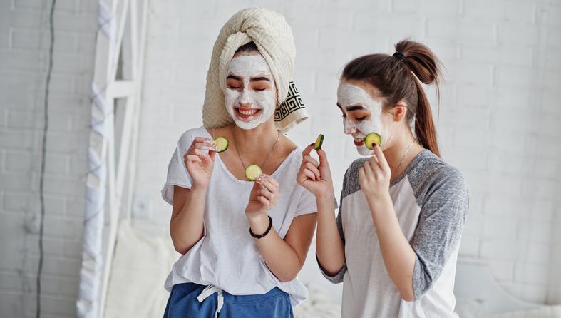 Two twins girls in pajamas with facial mask and cucumber slices.