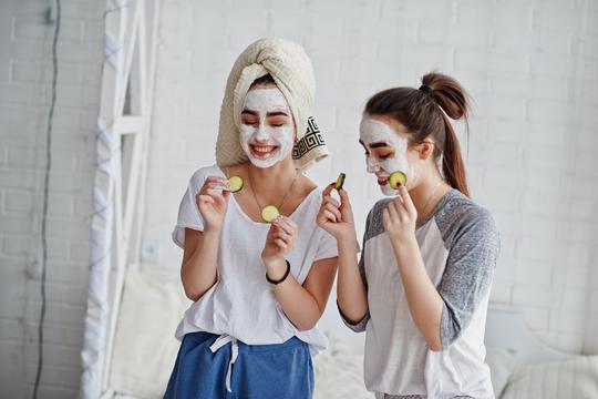 Two twins girls in pajamas with facial mask and cucumber slices.
