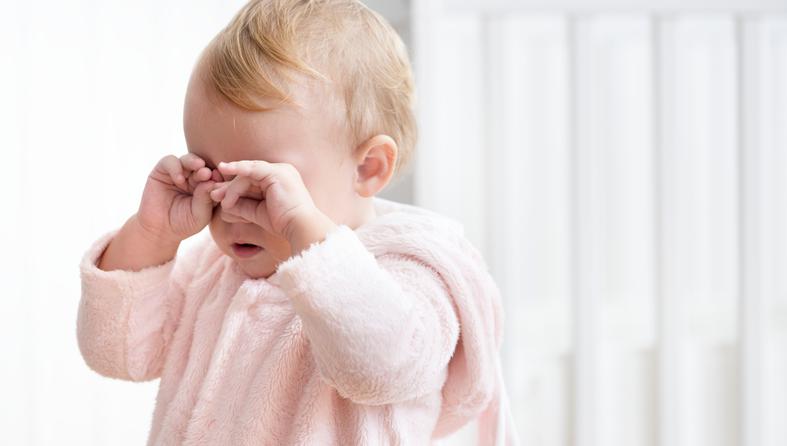 Tired baby girl crying and rubbing her eyes