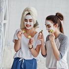 Two twins girls in pajamas with facial mask and cucumber slices.