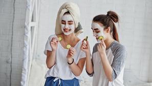 Two twins girls in pajamas with facial mask and cucumber slices.